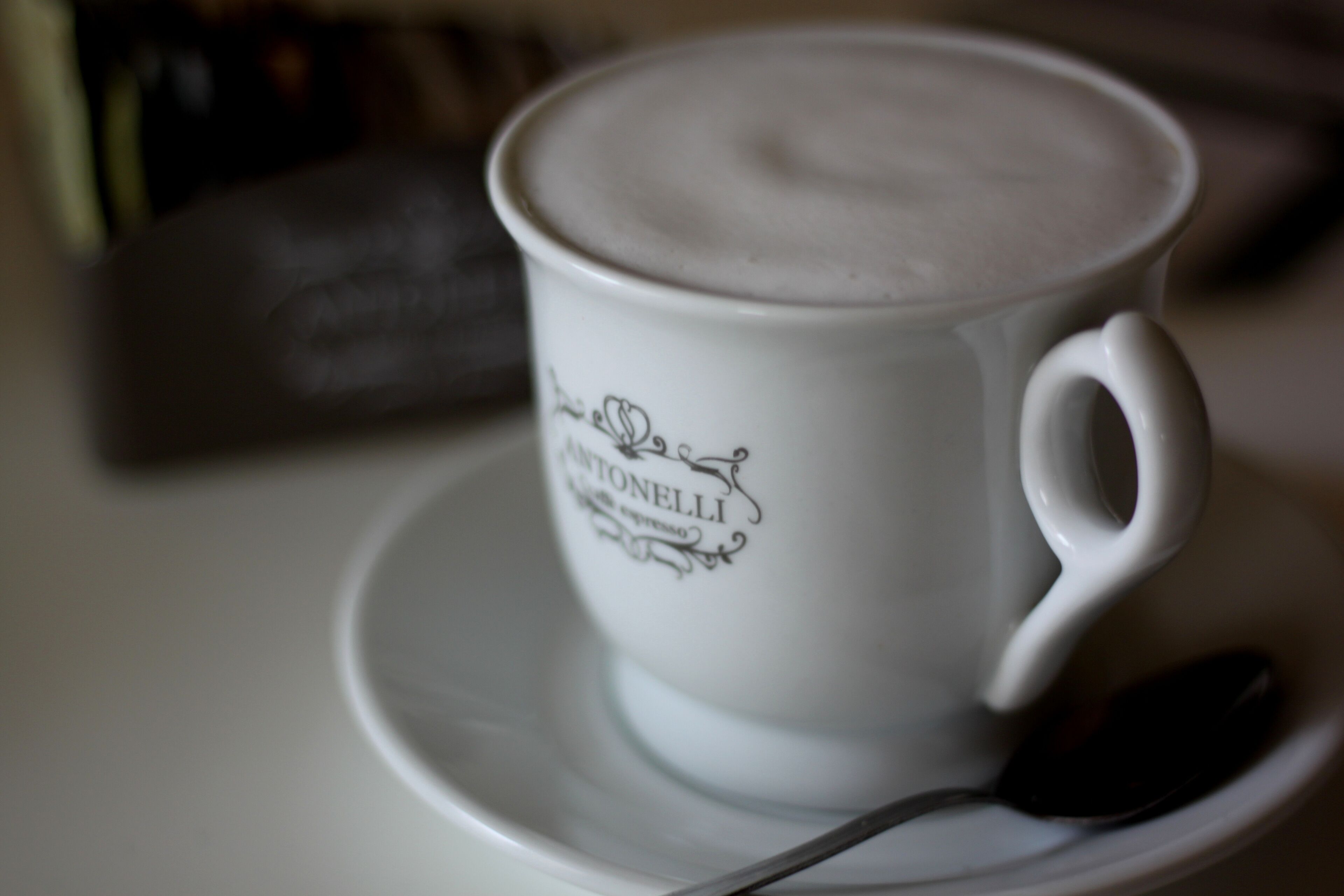 A white cup with "CANTONELLI" text and a spoon on a saucer.