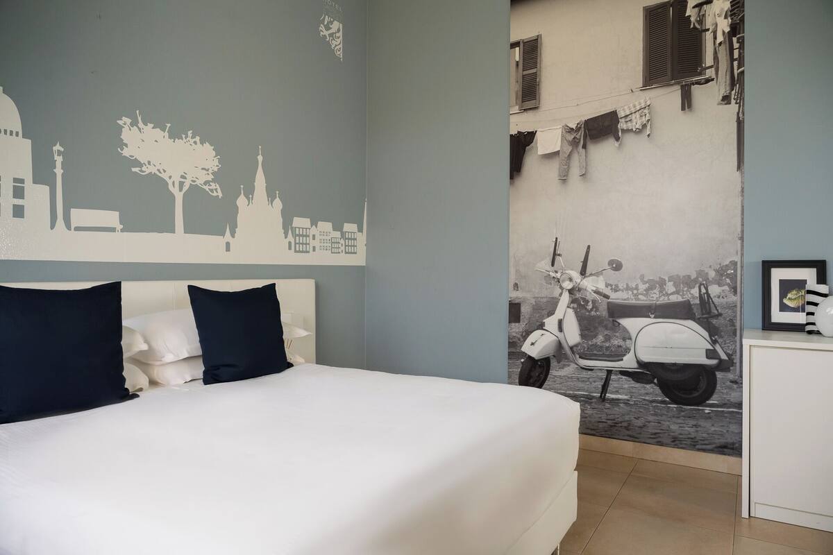 A bedroom with a bed, pillows, a wall mural, and a scooter.