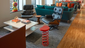 A modern hotel lobby with a teal sofa, black leather chairs, a wooden coffee table, and a red stool. - citizenM Amstel Amsterdam (Amsterdam)