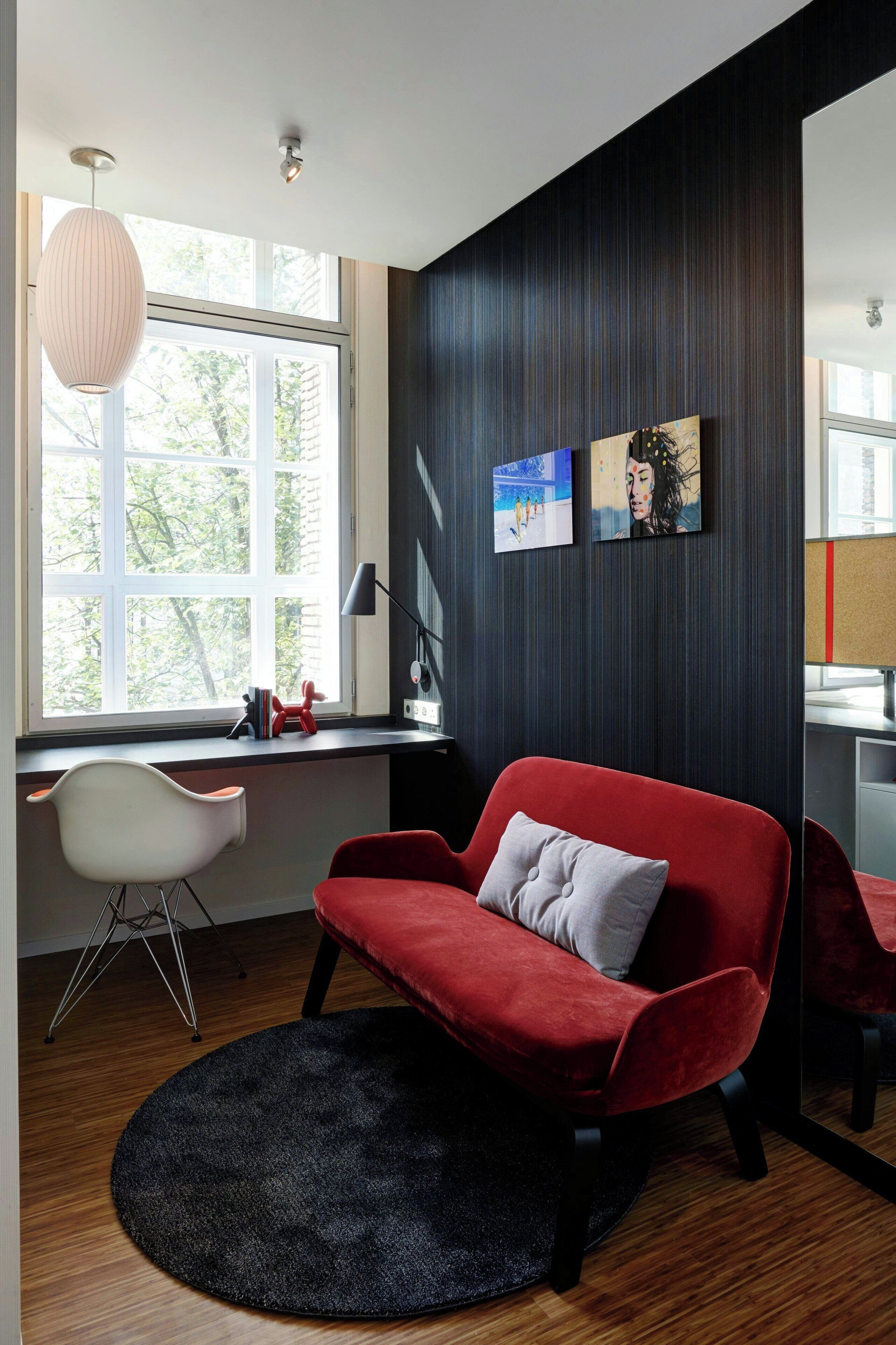 Una habitación moderna con un sofá rojo, una silla blanca, un tapete negro y obras de arte en la pared.