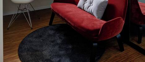 Une pièce moderne avec un canapé rouge, une chaise blanche, un tapis noir et des œuvres d’art accrochées au mur.