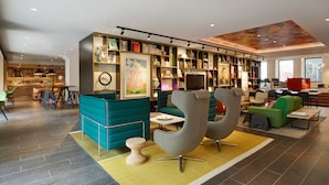 A modern interior with teal and gray seating, a bookshelf, and a vibrant ceiling mural. - citizenM Amstel Amsterdam (Amsterdam)
