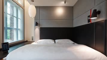 Et moderne soveværelse med en stor seng, et sengebord med en lampe og et vindue med persienner.