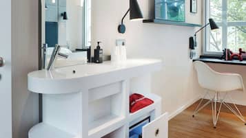 Un baño moderno con tocador blanco, un espejo grande, un lavabo y una ventana con vistas a árboles.