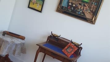 A room with a wooden table, a small table with a patterned tablecloth, and two framed artworks on the wall.