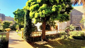 A courtyard with a wooden deck, a large tree, and a stone wall. - La Maison Blanche (Blaye)