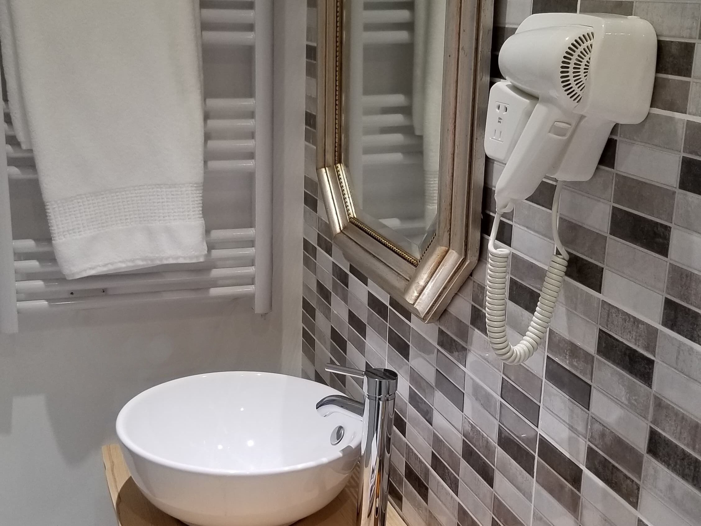 A bathroom with a white sink, a towel rack, a hairdryer, and a mirror with a decorative frame.