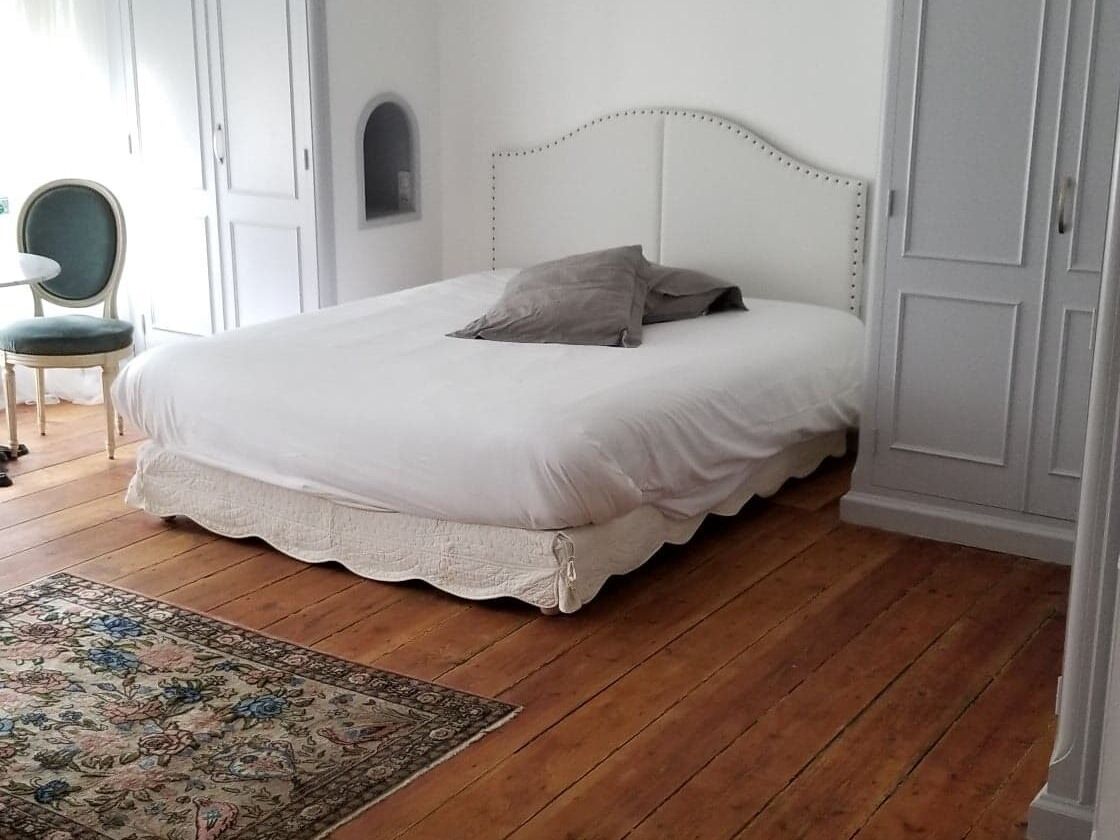 Een slaapkamer met een wit bed, een bloemenkleed en een groene stoel.