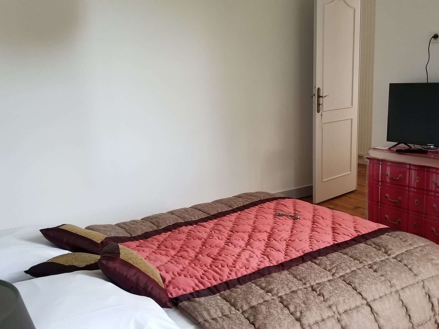 Um quarto com uma cama, uma televisão sobre um aparador e uma porta.