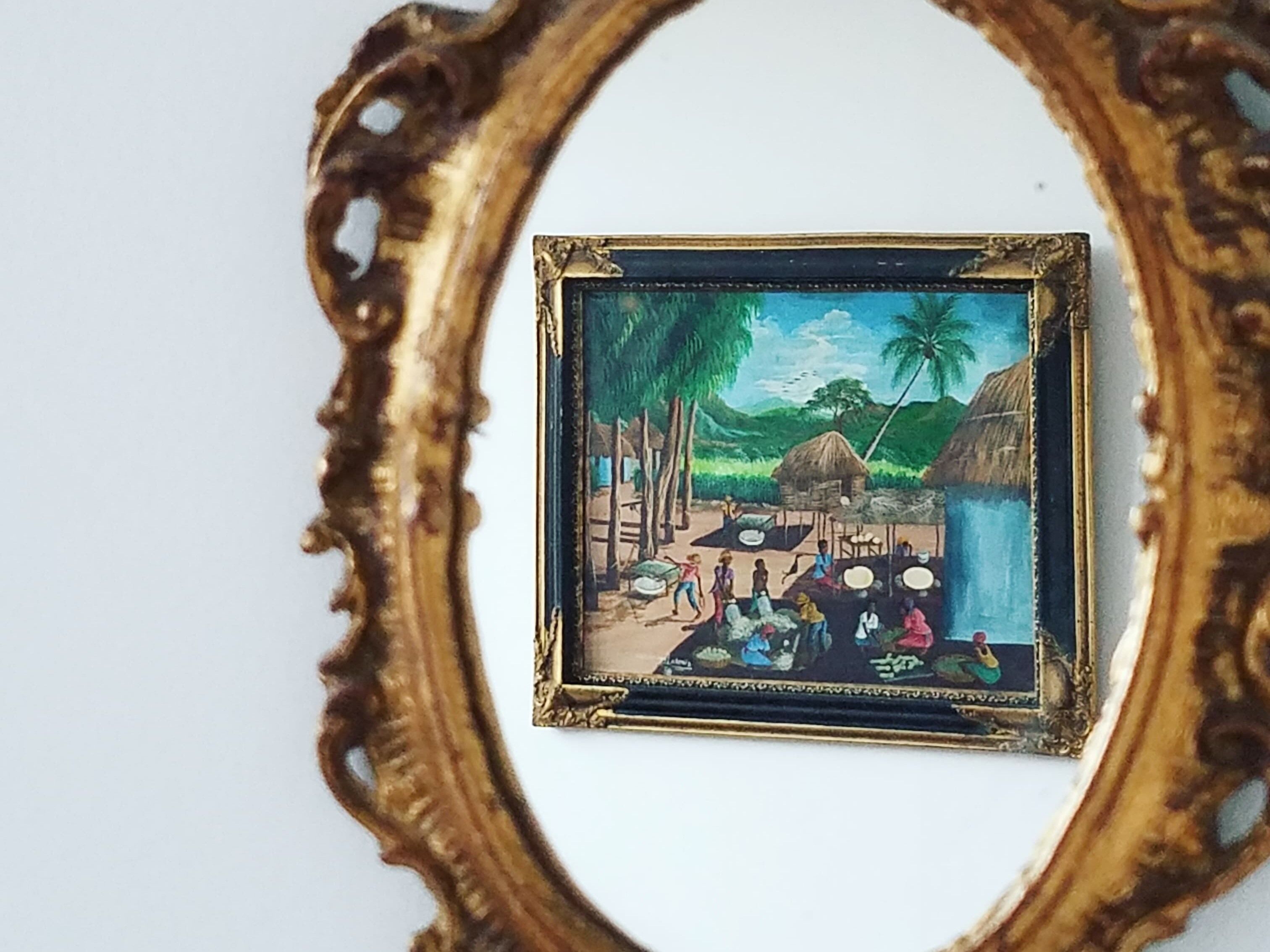 Un cuadro enmarco de una escena de un pueblo tropical con cabañas, palmeras y gente.