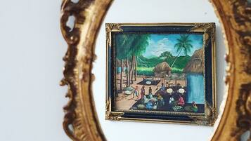 Un cuadro enmarco de una escena de un pueblo tropical con cabañas, palmeras y gente.