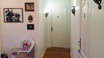 A hallway with a white door marked '2', a wicker chair with a cushion, and a wall adorned with framed pictures.