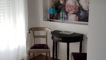 Una habitación con una silla, una mesita y un cuadro en la pared.