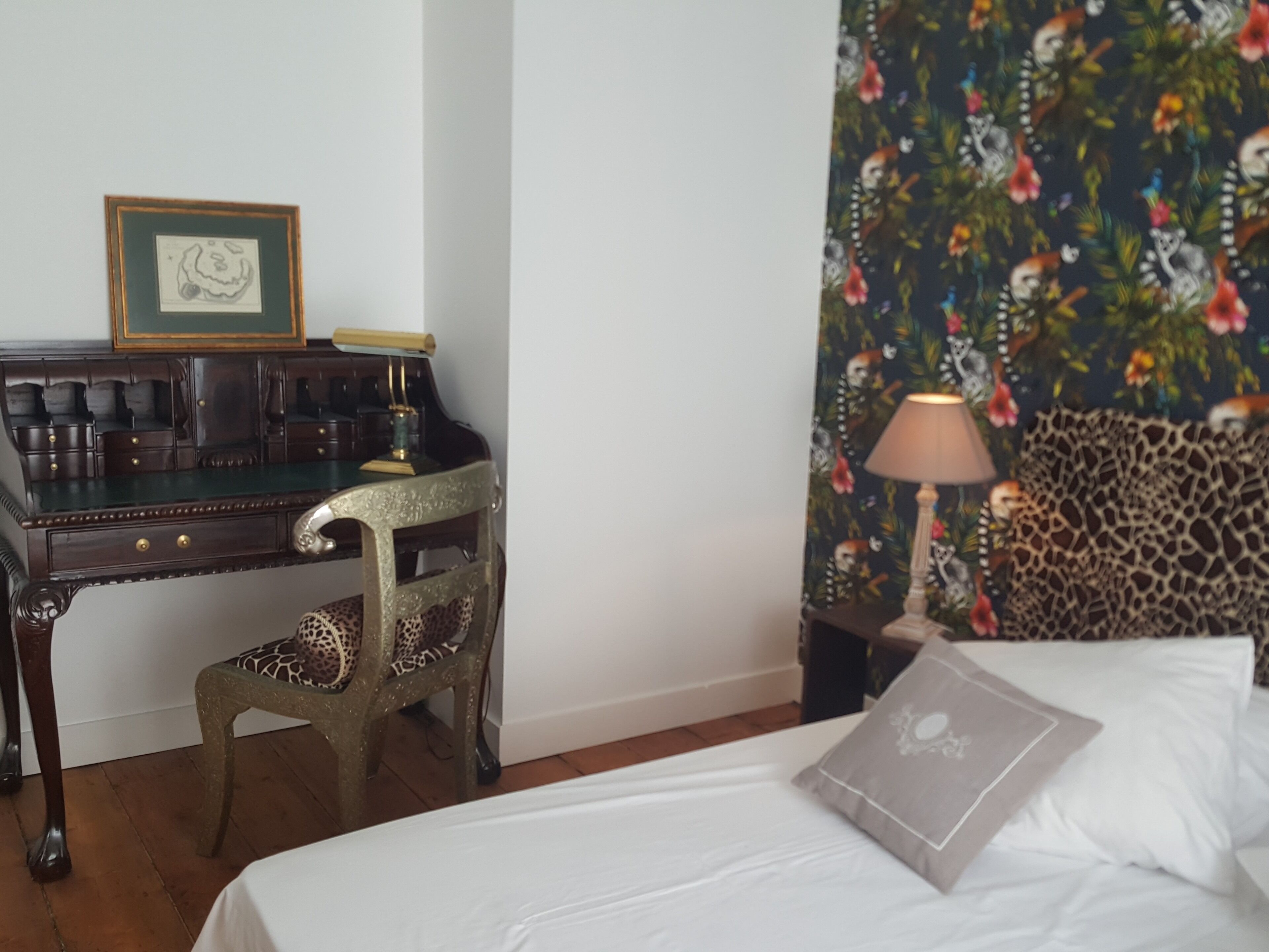 Una habitación de hotel con una cama, un escritorio con una silla, una lámpara y un cuadro en la pared.
