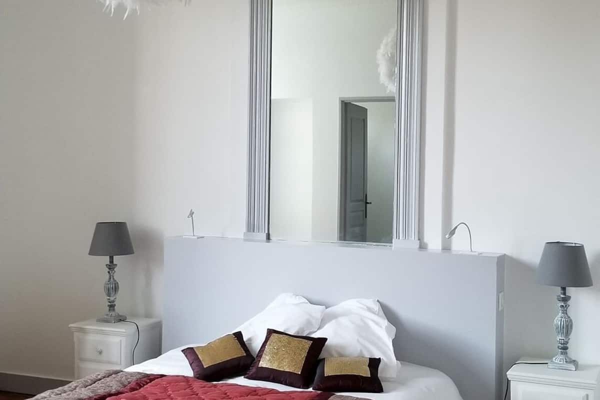 A bedroom with a large bed, two bedside tables with lamps, a mirror, and a fluffy white ceiling decoration.