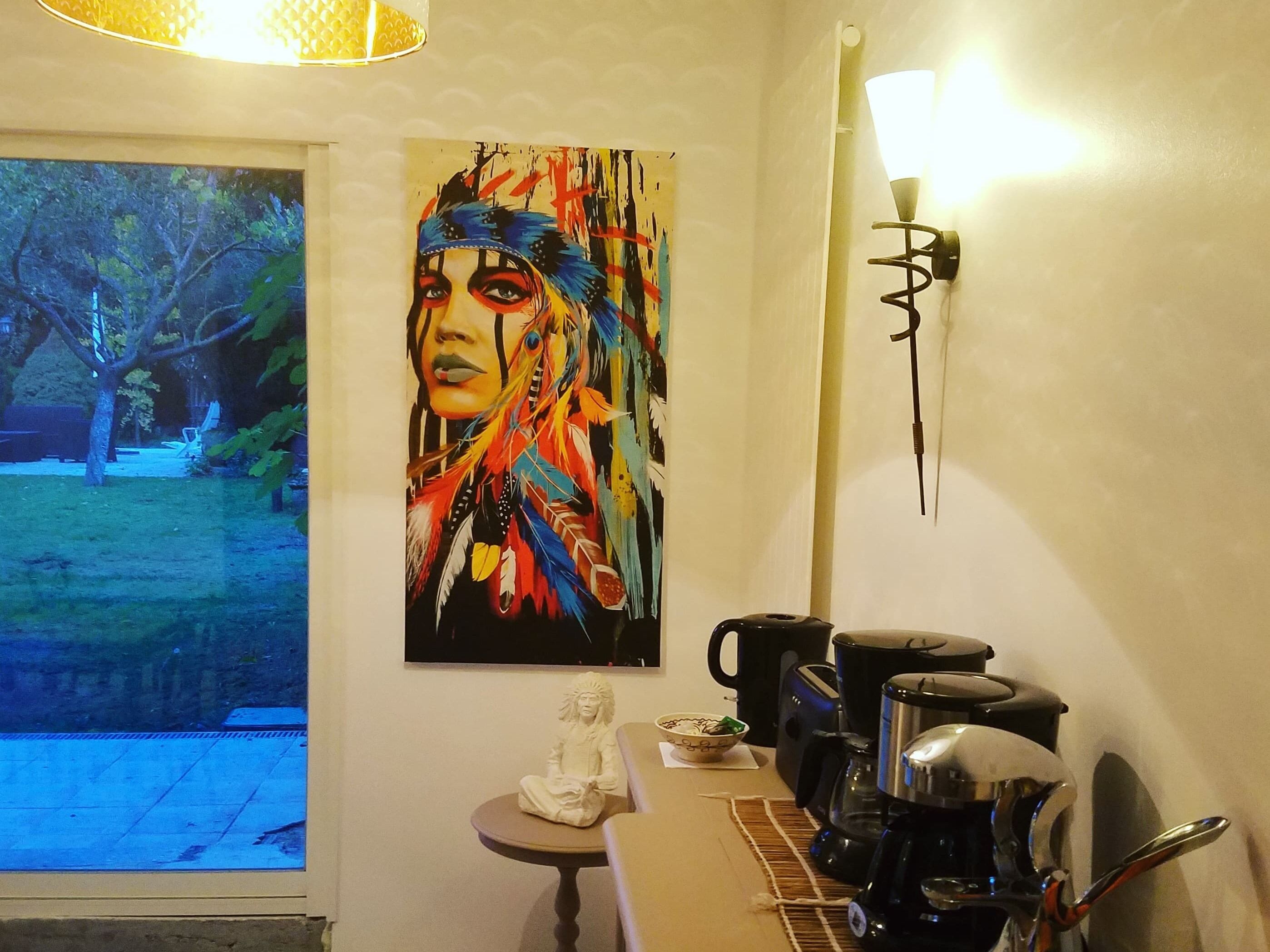A room with a large window, a painting on the wall, a coffee maker, and a small statue on a table.