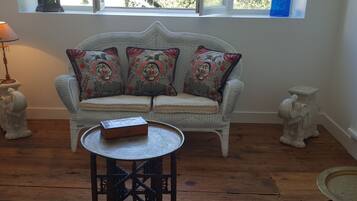 A wicker sofa with floral cushions, a small round table, and two decorative vases.