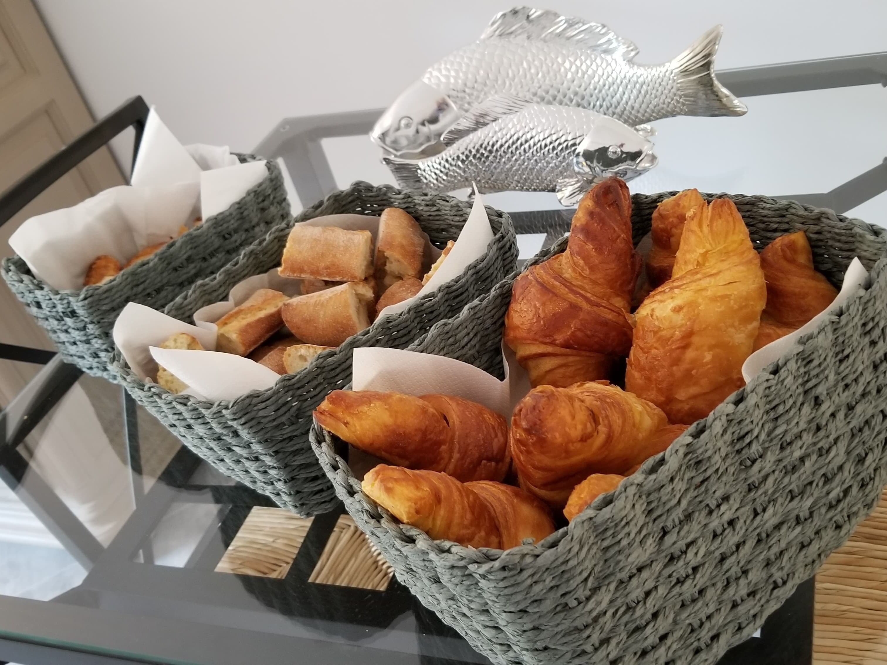 Two wicker baskets filled with bread and croissants on a glass table.