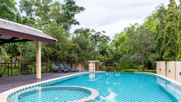 Una piscina con diseño de cuadros, rodeada de vegetación y un área cubierta con sillas de descanso.