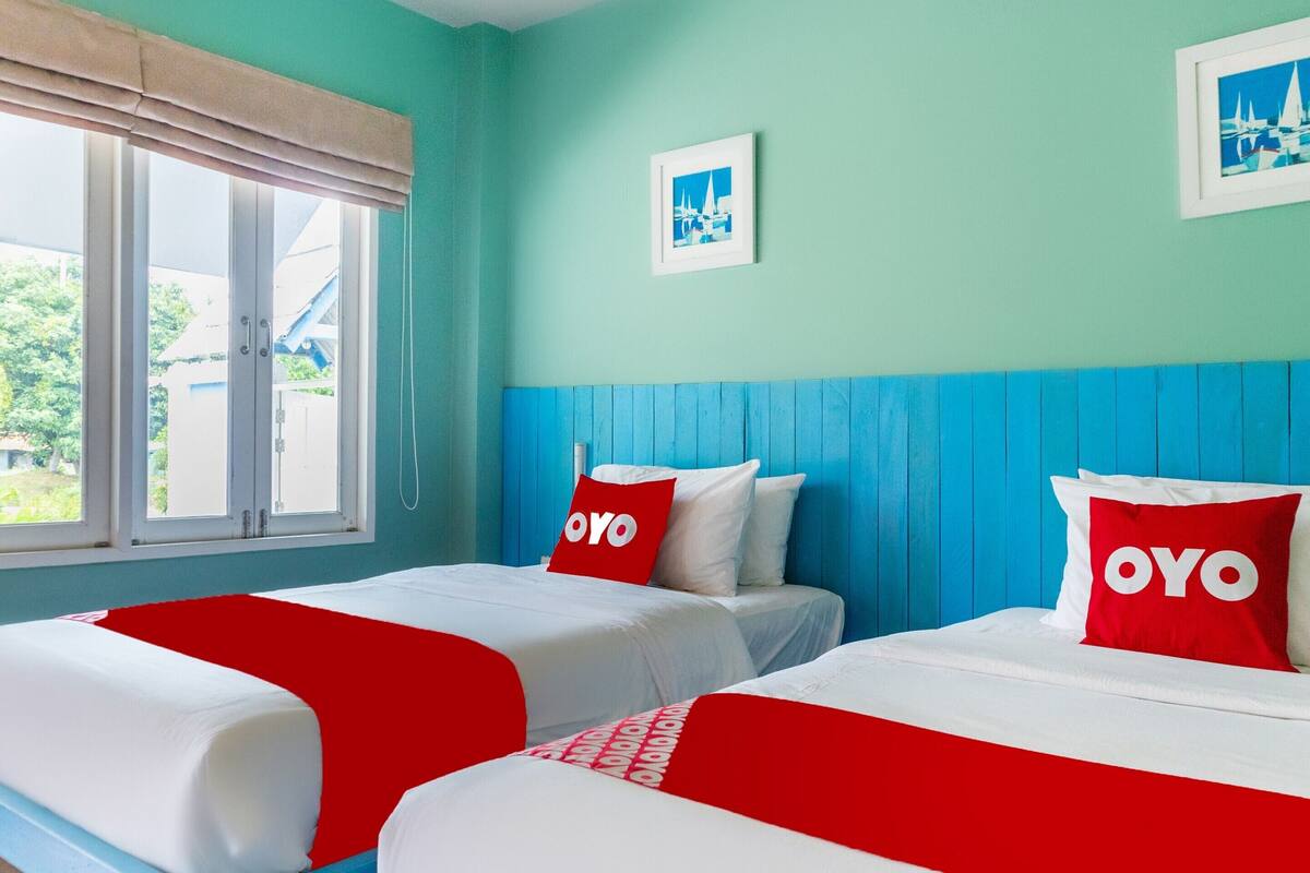 Ein Hotelzimmer mit zwei Betten, türkisfarbenen Wänden und einem Fenster mit Blick nach draußen.