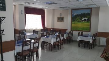 A dining area with multiple tables and chairs, a large window with a view of a landscape, and a framed certificate on the wall.