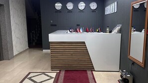 A reception area with a marble floor, a red patterned rug, a reception desk, and clocks displaying times from New York, London, Istanbul, and Tokyo. - Azizoglu Malkoc Hotel (Diyarbakir)