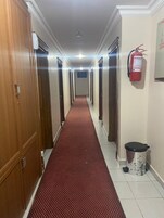 Pasillo de hotel con puertas de madera, alfombra roja, extintor y cesto de basura.