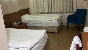 A hotel room with two beds, a wooden headboard, a blue armchair, a wooden dresser, and a curtain. - Azizoglu Malkoc Hotel (Diyarbakir)