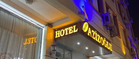 Ett hotell med en skylt där det står ”HOTEL AZIZOGLU” och en väl synlig entré med en krukväxt utanför.