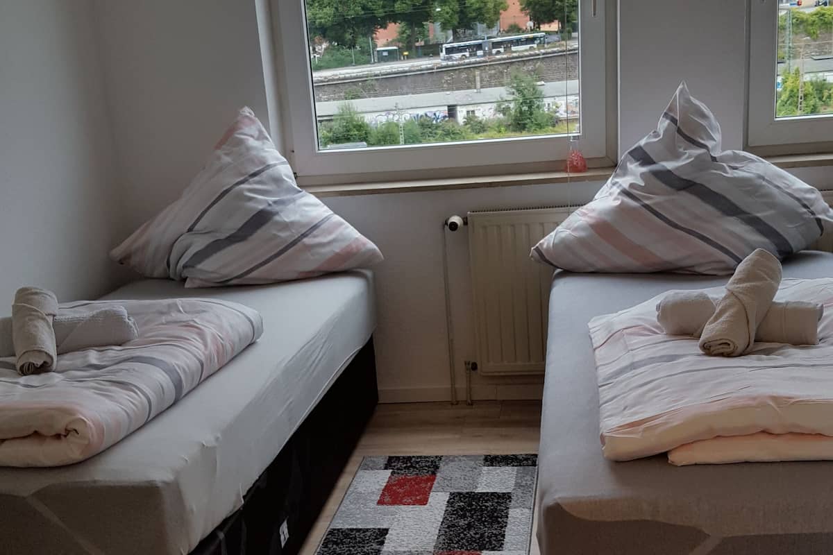 Ein Schlafzimmer mit zwei Betten, Blick auf die Stadt durch große Fenster und einem gesteppten Teppich auf dem Boden.