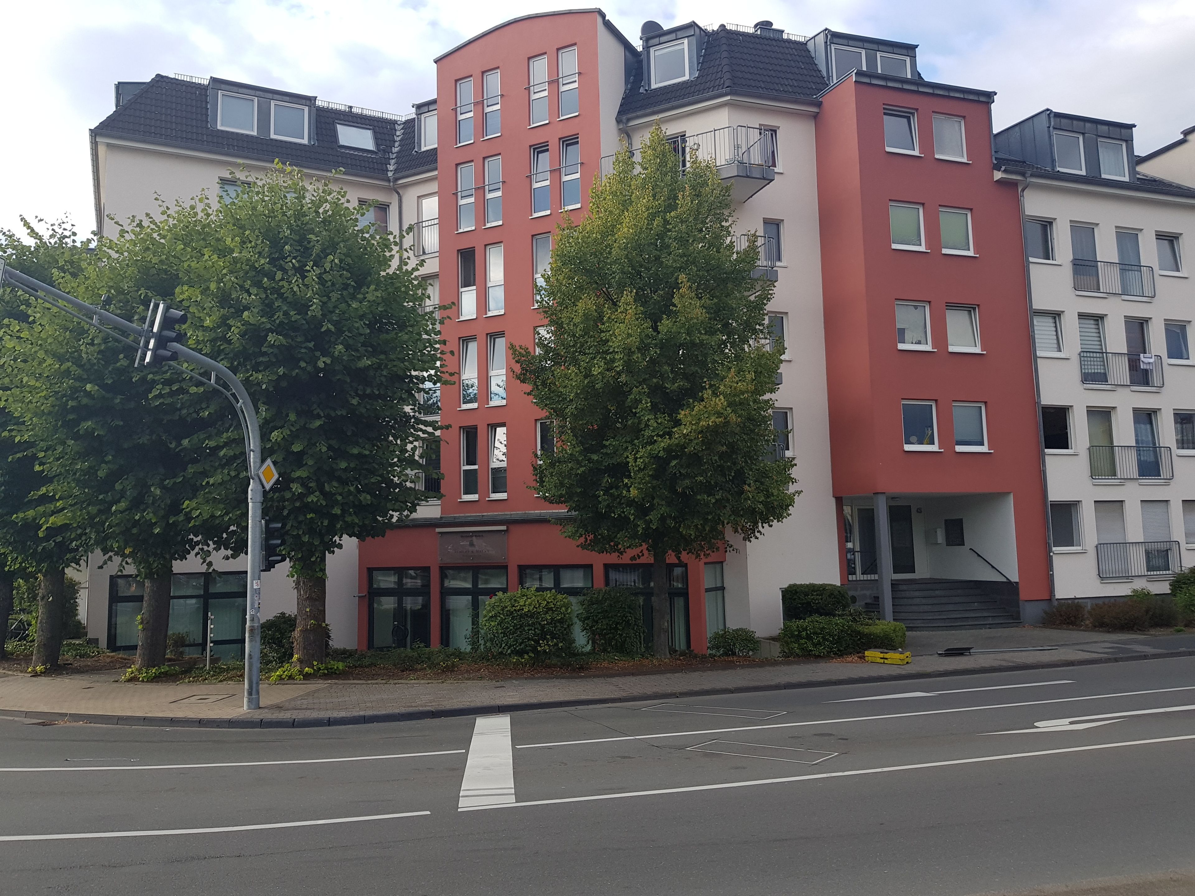 En byggnad med flera våningar, en röd och vit fasad, stora fönster och en tydligt markerad entré med trappsteg.