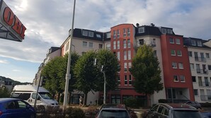 Ein mehrstöckiges Gebäude mit Wohn- und Geschäftsräumen, das eine auffällige rote Fassade und mehrere Balkone aufweist.