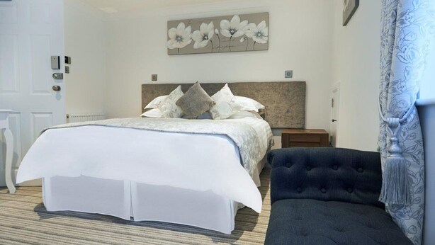 A bedroom with a bed, a dark upholstered chair, and a wall-mounted artwork. - The Rose & Crown Free House (Clacton-on-Sea)
