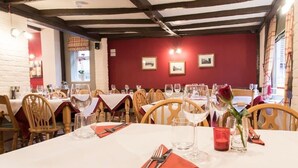 A dining area with tables set for two, wooden chairs, and a red wall with framed pictures. - The Rose & Crown Free House (Clacton-on-Sea)