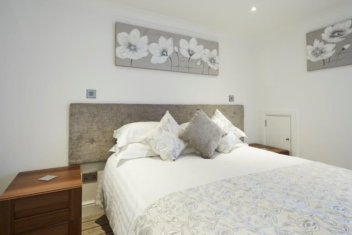 A bedroom with a large bed, a headboard, a nightstand, a wooden dresser, and two wall-mounted flower paintings.