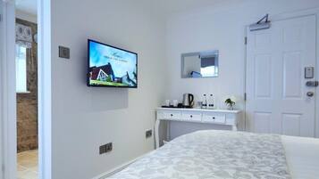 A hotel room with a bed, a TV mounted on the wall, a desk with a mirror, and a door.