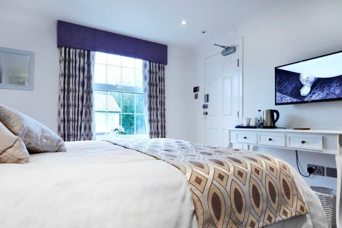 A modern bedroom with a large bed, a television on the wall, and a window with curtains.