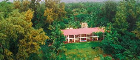 A two-story building with a red roof, surrounded by dense greenery and a small pond.