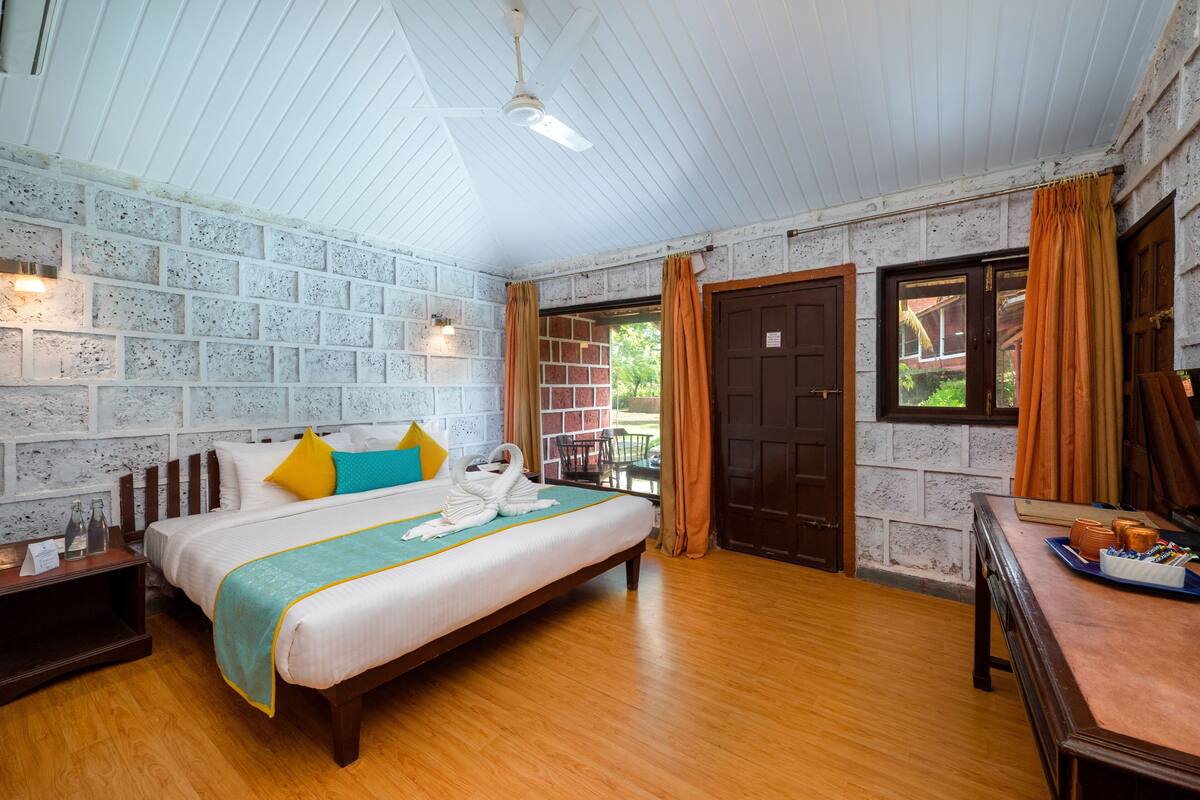 Une chambre d’hôtel avec un grand lit, un plancher en bois, des murs en briques peintes en blanc et un ventilateur de plafond.