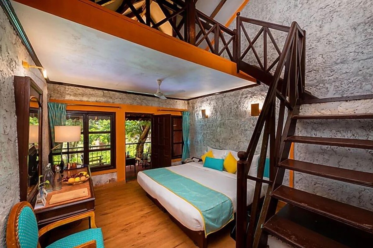 Ein Schlafzimmer mit Bett, Schreibtisch, Stuhl, einer Treppe und Blick auf Grünflächen.