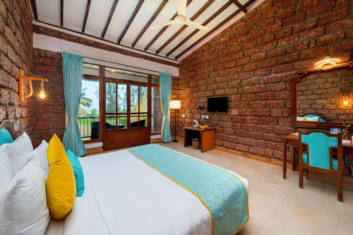 Une chambre d’hôtel avec un mur en briques, un grand lit recouvert d’une courtepointe bleue et blanche, un bureau en bois avec une chaise et un téléviseur fixé au mur.