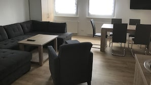 Una sala de estar moderna con un sofá modular, una mesa de comedor con sillas y un televisor montado en la pared.