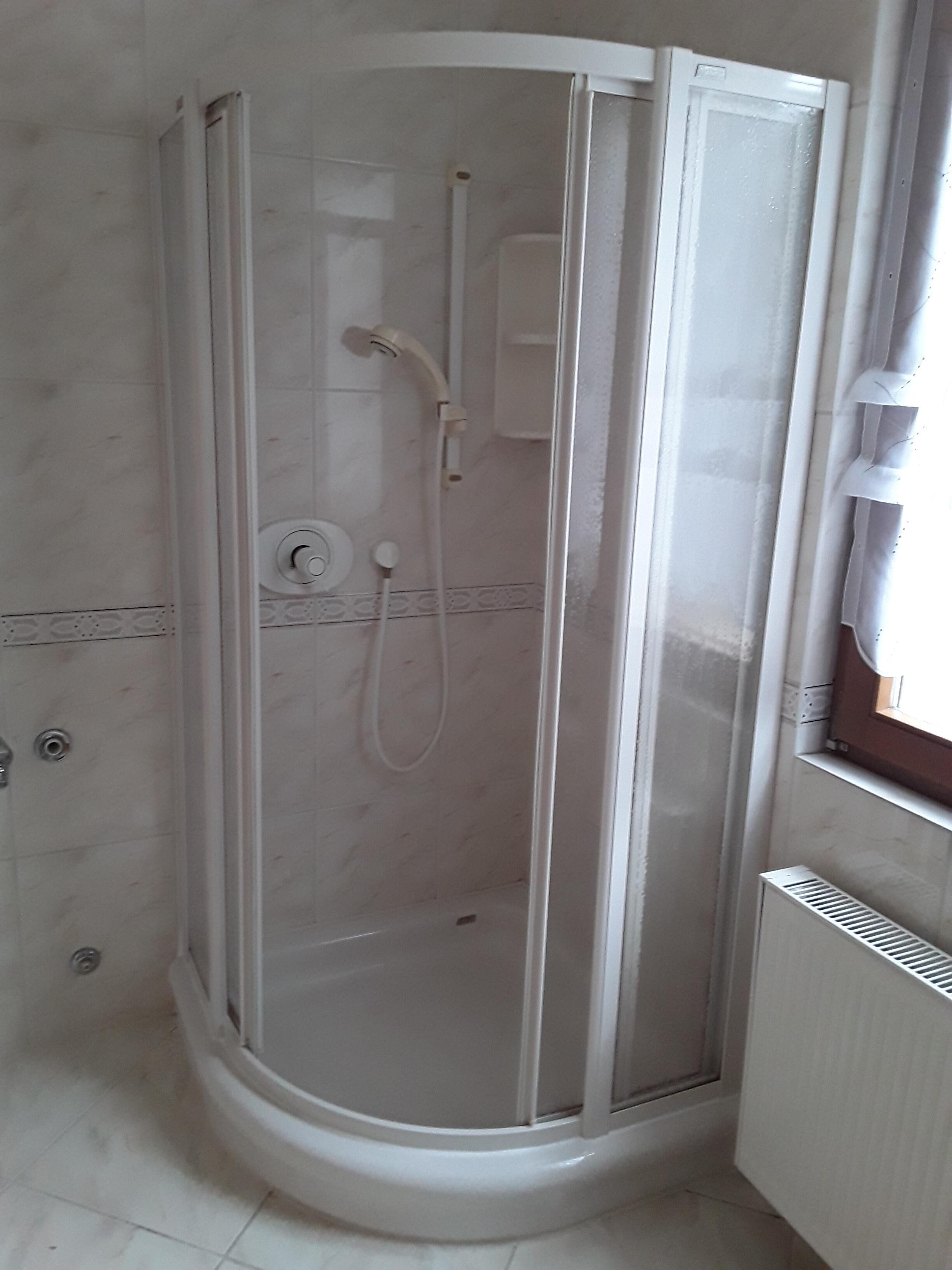A corner shower with a glass door, a handheld showerhead, and a wall-mounted control panel.