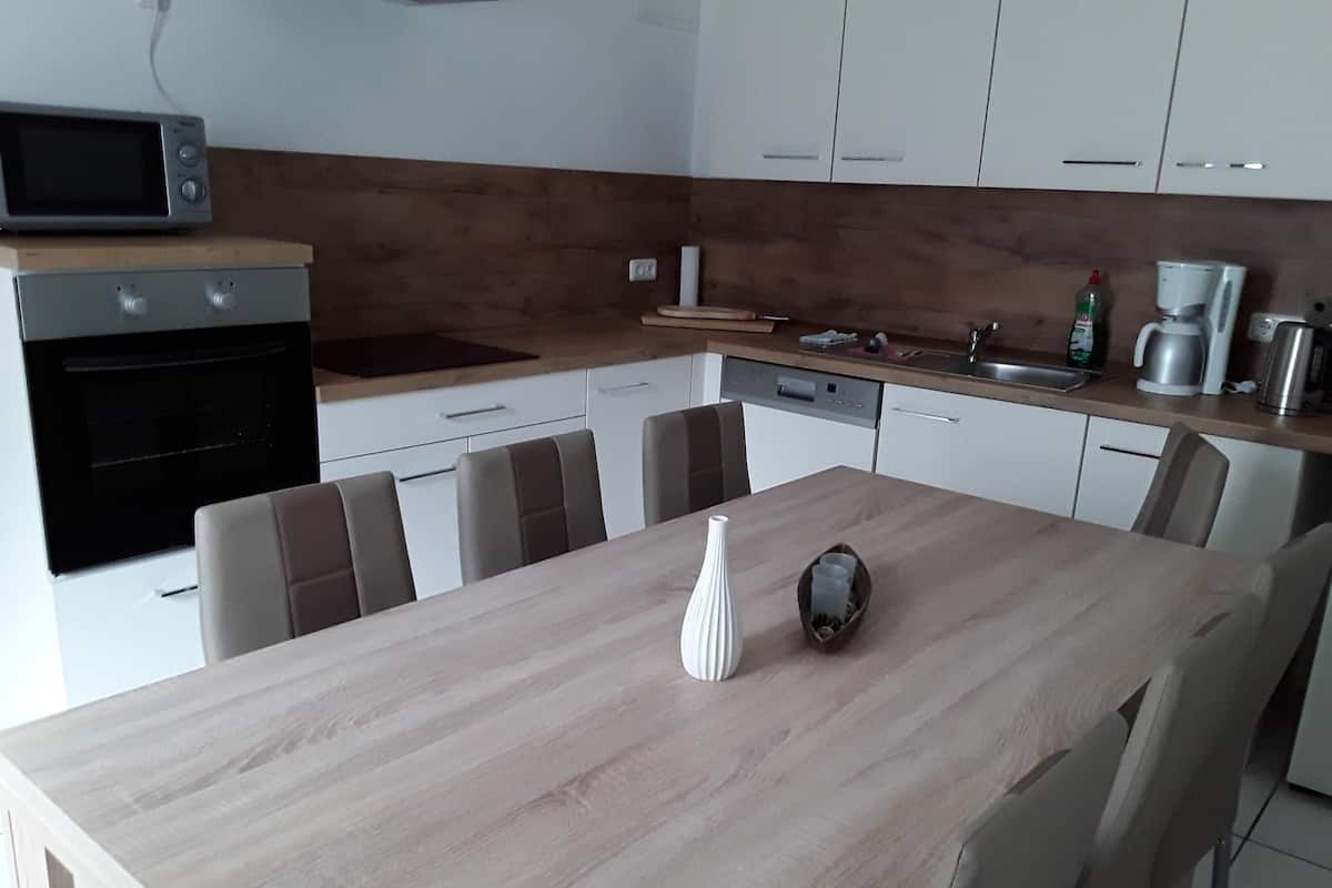 A modern kitchen with a wooden table, white cabinets, a microwave, and a coffee maker.