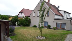 Una casa moderna con un césped cuidado, un árbol pequeño y un camino pavimentado que conduce a una estructura de madera.