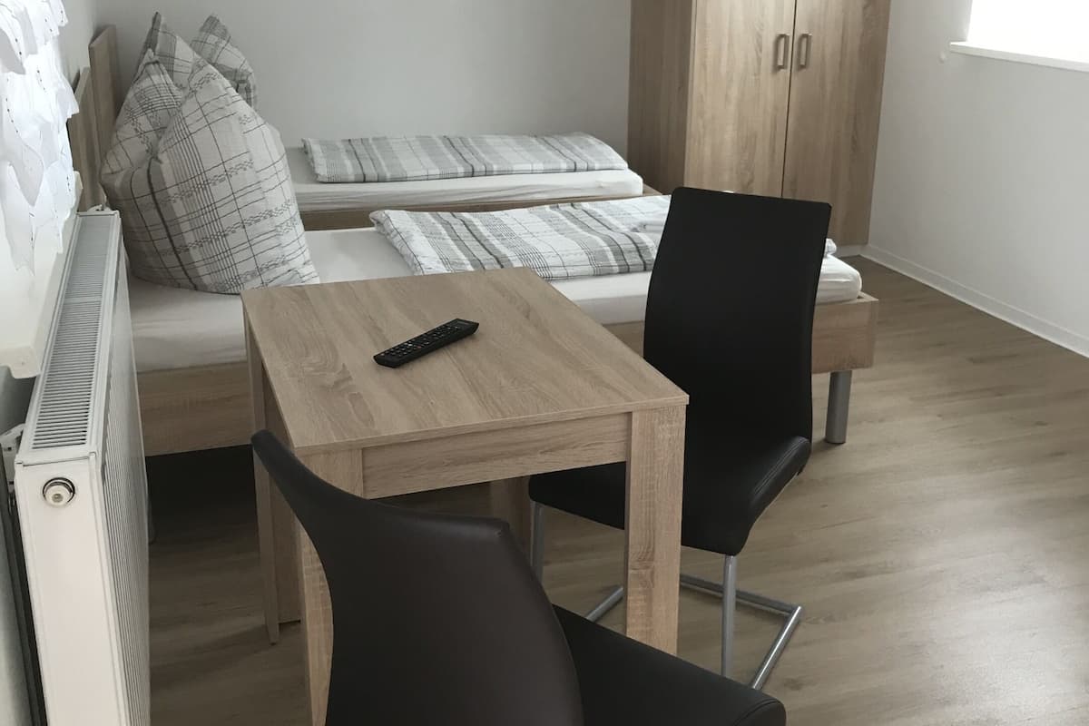 A compact living space with a bed, a small table, two chairs, a wardrobe, and a radiator.