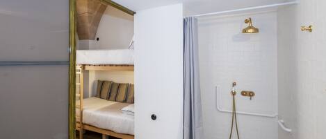 A compact room with a bunk bed, a shower with a golden showerhead, and white tiled walls.
