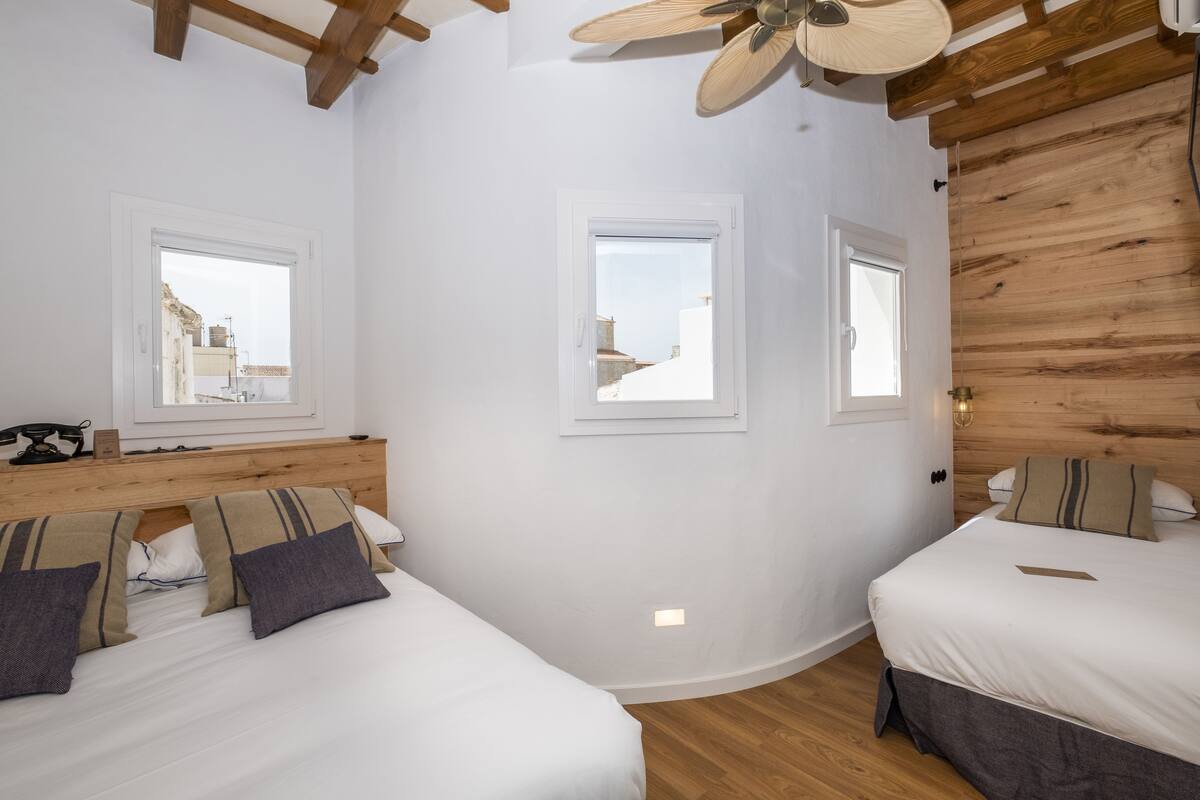 A bedroom with two beds, wooden ceiling beams, and a ceiling fan.