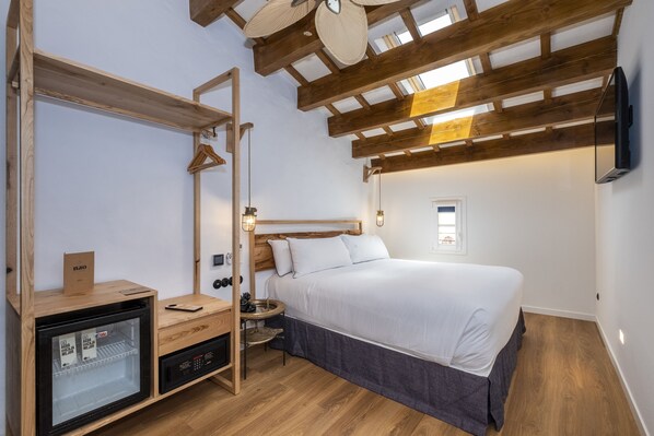 Un dormitorio con cama, vigas de madera en el techo, una mesita de noche, un armario y un mini refrigerador empotrado.