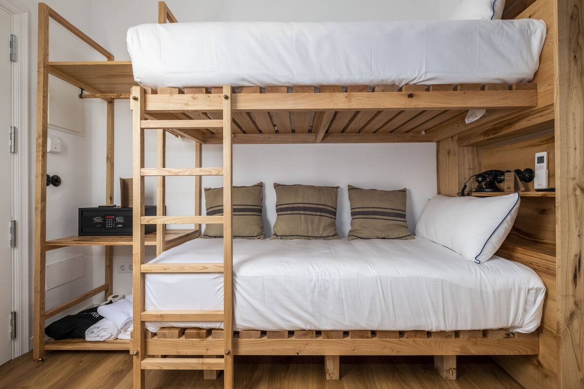 A bunk bed with a wooden ladder, a bedside table with a radio, and a shelf with a camera and a phone.